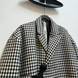 Close up frontside oversized double breasted, light padded wool jacket in black and white baker check, closing with hidden buttons and two long straps