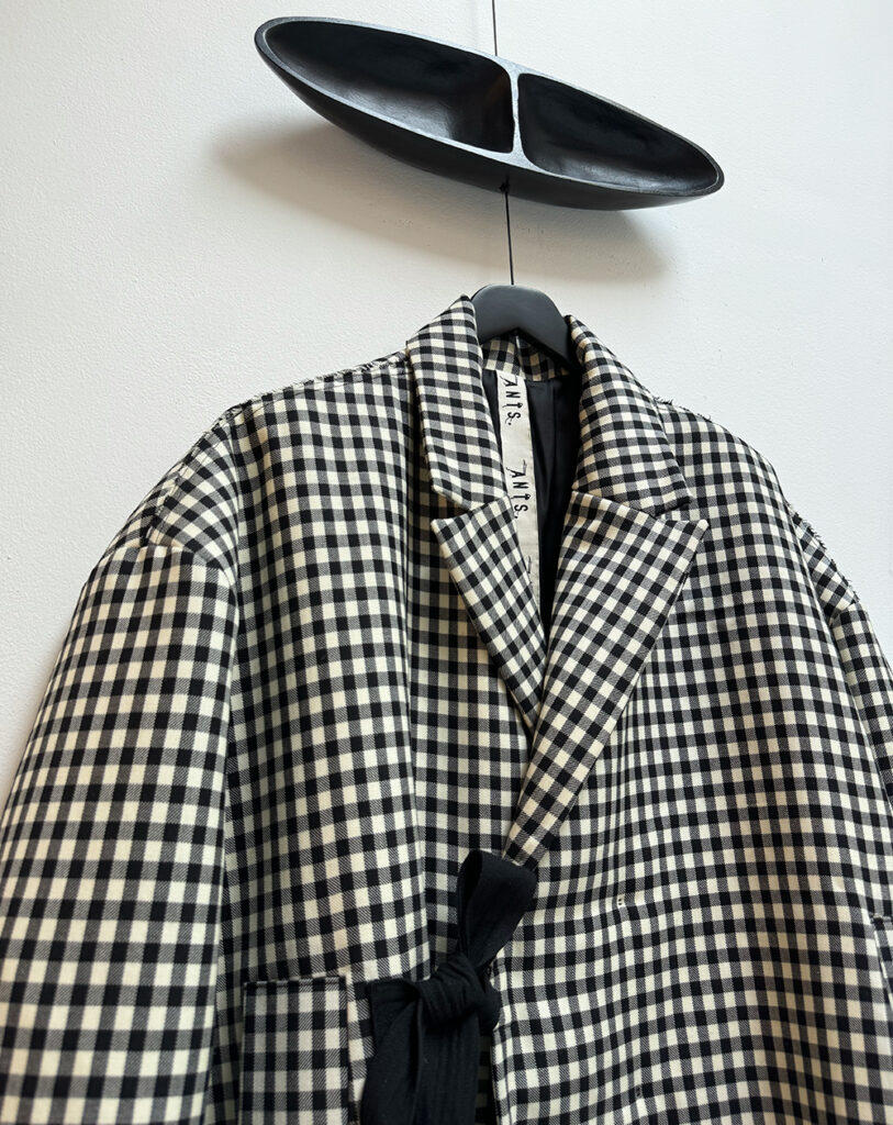 Close up frontside oversized double breasted, light padded wool jacket in black and white baker check, closing with hidden buttons and two long straps