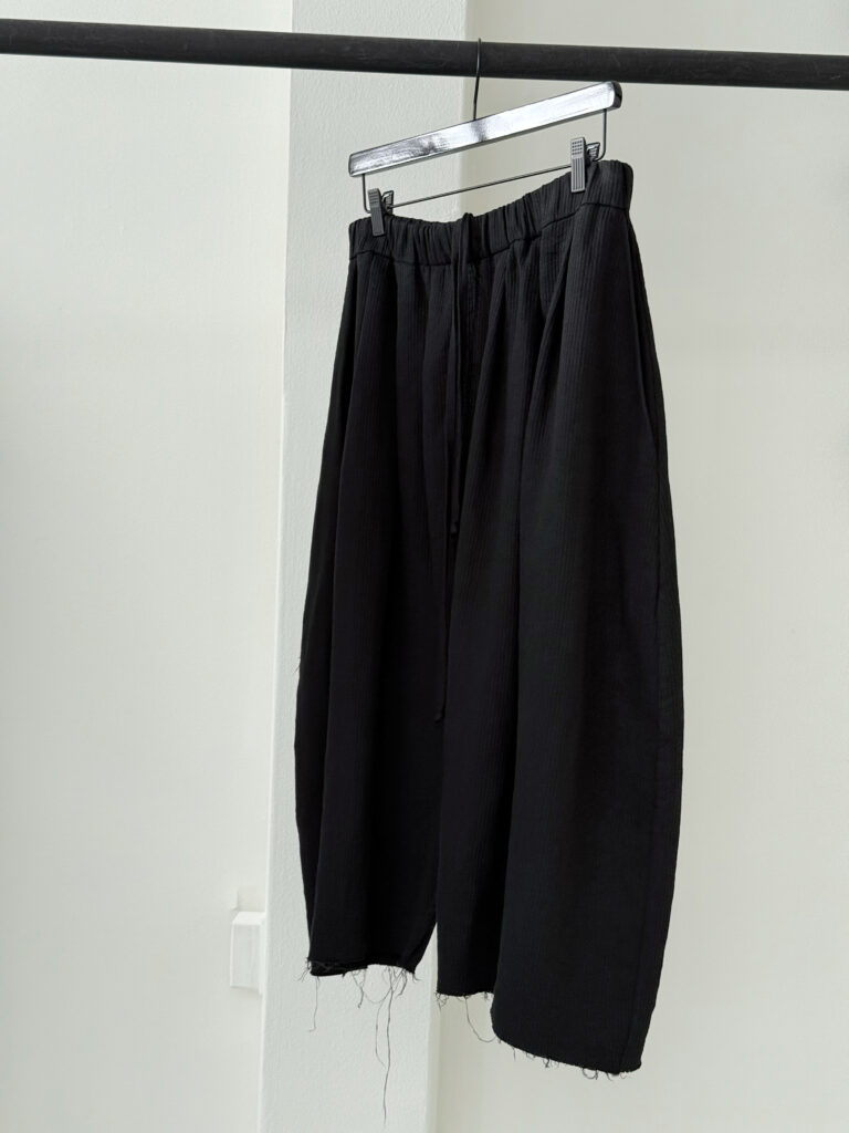 Sideview of round shaped culottes with multiple waistband pleats made in black Japanese linen corduroy fabric